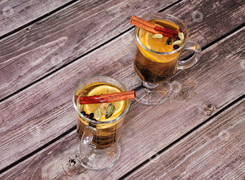 Скачать На деревянном столе стоят два стакана травяного чая с ломтиком лимона, корицей и специями. фотосток Ozero