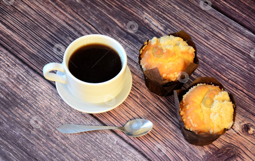 Скачать Два свежих кекса с посыпкой и чашка черного кофе на блюдце с ложечкой на деревянном столе. фотосток Ozero