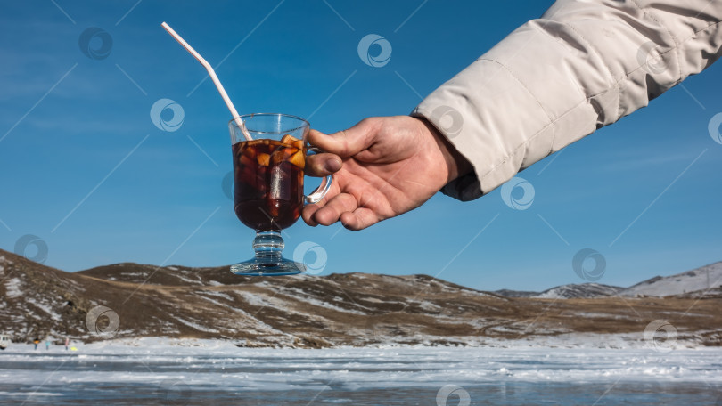 Скачать Бокал с горячим глинтвейном в руке мужчины на фоне зимнего пейзажа. фотосток Ozero