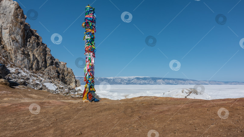 Скачать На берегу замерзшего озера, на голой земле, стоит деревянный ритуальный столб, перевязанный яркими разноцветными лентами. фотосток Ozero