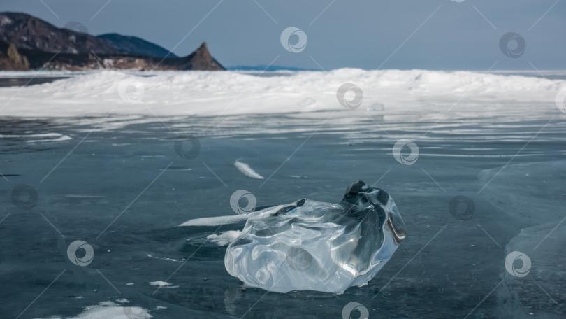 Скачать Блестящий прозрачный осколок льда причудливой формы лежит на поверхности замерзшего озера. фотосток Ozero