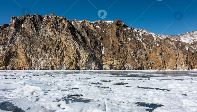 Скачать Живописный горный хребет, лишенный растительности и покрытый снегом, возвышается над ледяным озером. фотосток Ozero