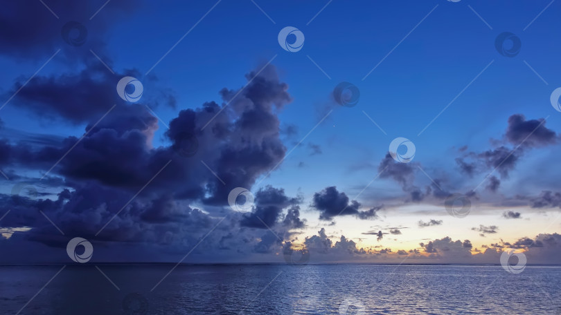 Скачать Фантастический закат на Мальдивах. Живописные кучевые фиолетовые облака на фоне голубого неба. фотосток Ozero