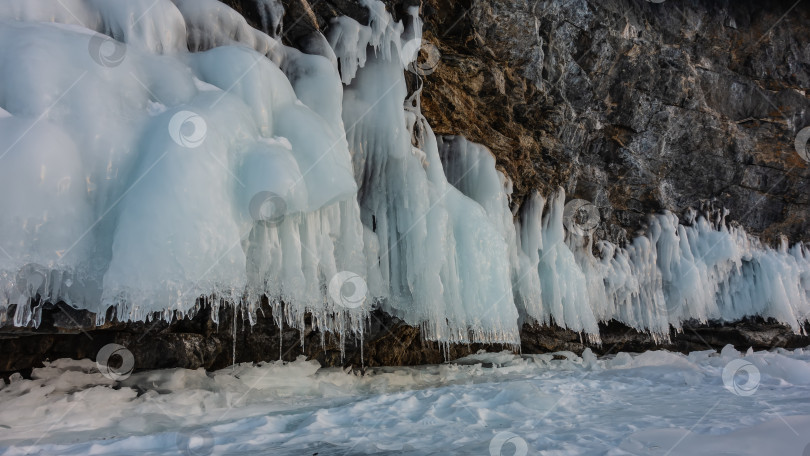 Скачать Гранитная скала у основания покрыта ледяными брызгами, сосульками, похожими на кружевные оборки.Озеро Байкал зимой. фотосток Ozero