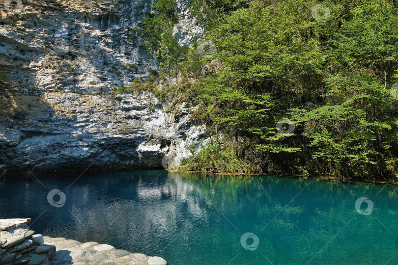 Скачать Спокойное бирюзовое озеро окружено скалами с зеленой растительностью. Голубое озеро. Абхазия фотосток Ozero