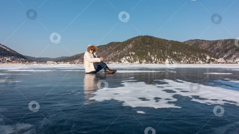 Скачать Мужчина в пуховике сидит на замерзшем озере. Отражение на льду.   Байкал фотосток Ozero