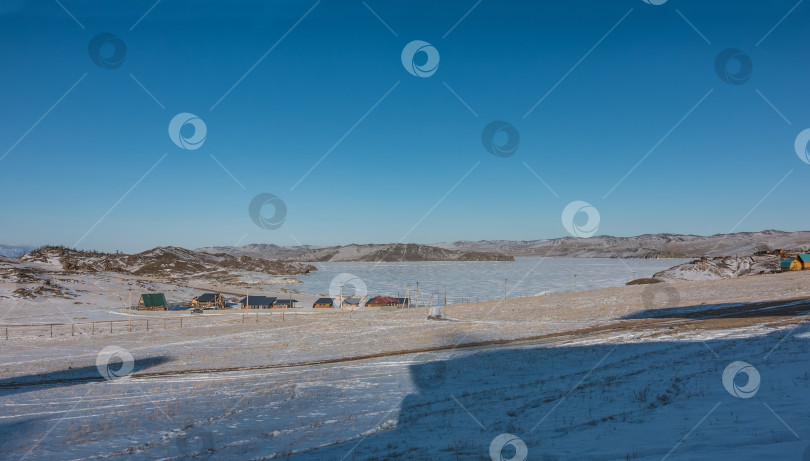 Скачать Замерзшее озеро окружено горами. На заснеженном берегу стоят деревянные дома фотосток Ozero