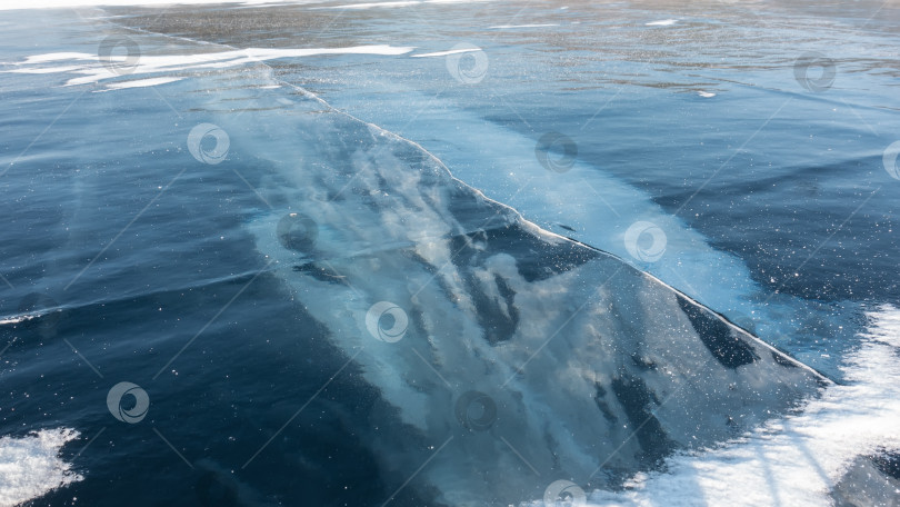 Скачать Гладкую голубую поверхность замерзшего озера пересекает глубокая трещина. Озеро Байкал зимой фотосток Ozero