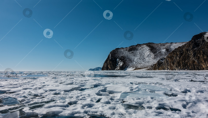 Скачать На замерзшем озере лежит снег и льдины. Гранитные скалы на фоне голубого неба. Байкал фотосток Ozero
