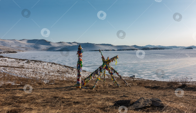 Скачать Замерзшее озеро окружено горами. На берегу установлены деревянные столбы, перевязанные разноцветными ритуальными лентами. фотосток Ozero