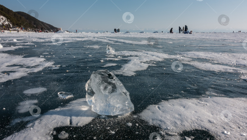Скачать Прозрачный осколок льда лежит на замерзшем озере. Солнечные блики по краям, тень на снегу. фотосток Ozero