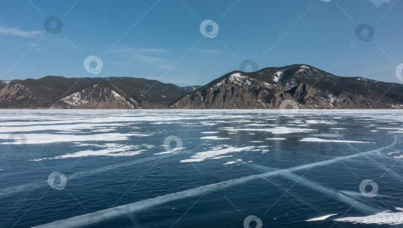 Скачать Замерзшее озеро покрыто пересекающимися трещинами. Участки снега на голубом льду. фотосток Ozero