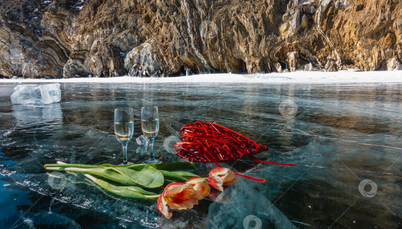 Скачать На замерзшем озере стоят два бокала с шампанским, красные и желтые тюльпаны, декоративное плетеное сердечко фотосток Ozero