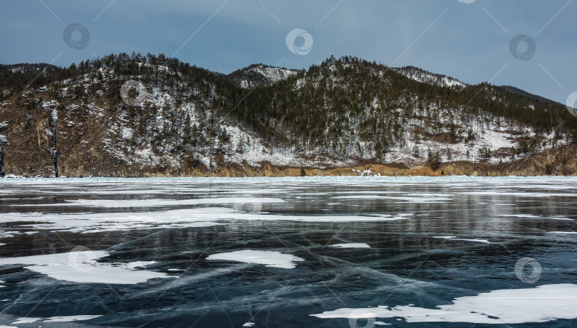Скачать На голубом льду замерзшего озера видны пересекающиеся трещины и участки снега.  Байкал фотосток Ozero