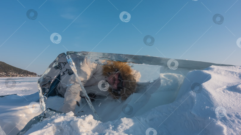 Скачать Толстая льдина на замерзшем озере окружена сугробами снега.. Человек лежит на снегу, смотрит сквозь прозрачный лед. фотосток Ozero