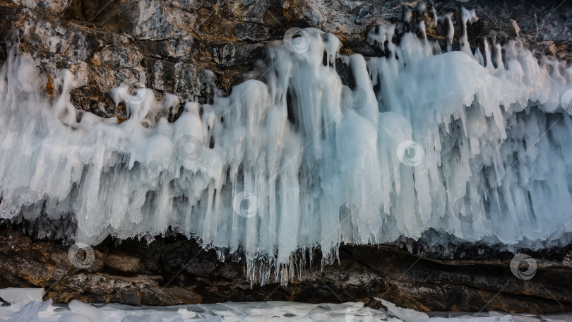 Скачать Причудливые сосульки на склоне отвесной гранитной скалы. Кружево льда над замерзшим озером. фотосток Ozero