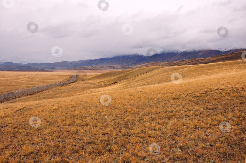 Скачать Склон холма в осенней степи, окруженный горами с заснеженными вершинами. фотосток Ozero