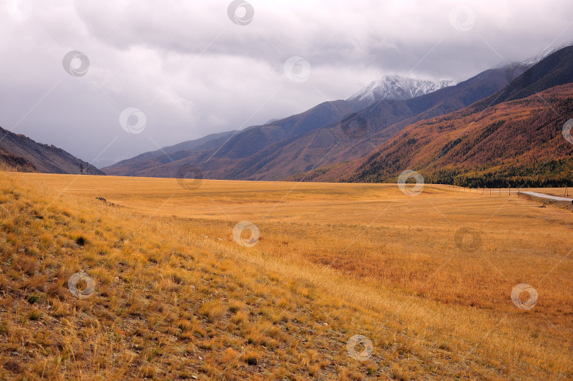 Скачать Узкая долина осенью, окруженная горными вершинами в грозовых облаках. фотосток Ozero