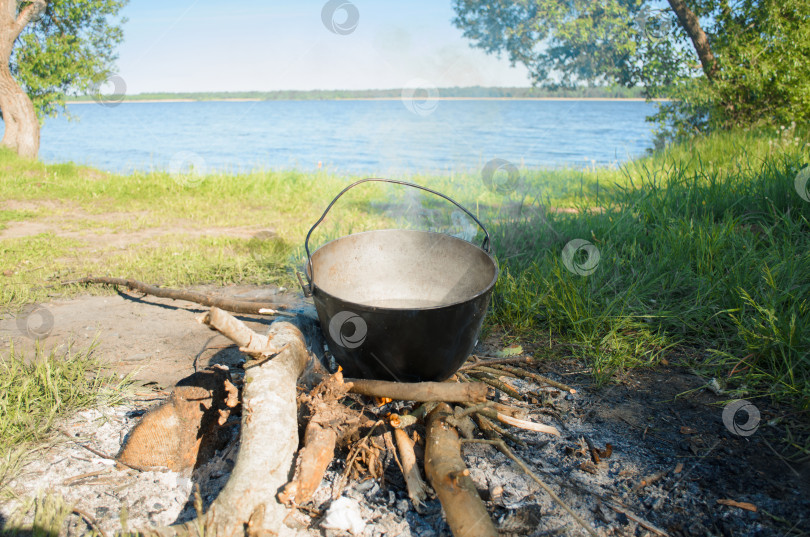 Скачать Поход на природу. Приготовление пищи в кастрюле на огне солнечным летним днем. Походная еда на берегу озера. фотосток Ozero