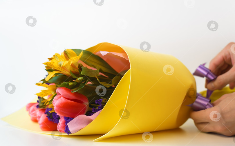 Скачать Флорист делает подарочный букет цветов. Руки завязывают ленту на букете тюльпанов и лилий. Выборочный фокус на переднем плане фотосток Ozero