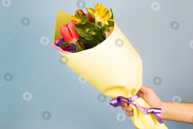 Скачать Мужская рука держит украшенный букет цветов. Мужчина дарит цветы в желтой оберточной бумаге в помещении. фотосток Ozero