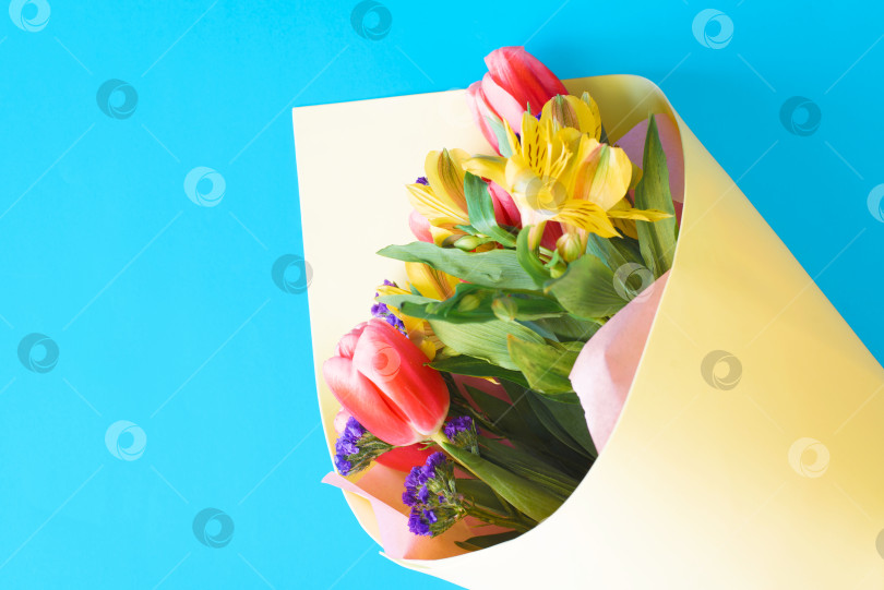 Скачать Оформленный букет весенних цветов на синем фоне, вид сверху. Тюльпаны и лилии в желтой подарочной бумаге фотосток Ozero