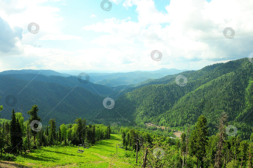 Скачать Вид с вершины горы на высокие холмы, поросшие лесом, и канатную дорогу кресельного подъемника, спускающуюся в долину. фотосток Ozero