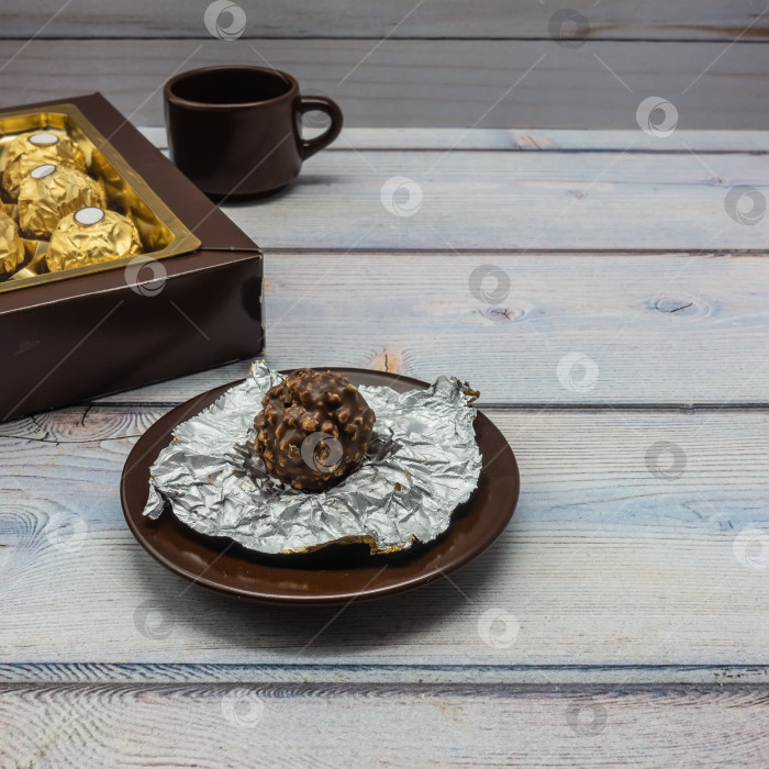 Скачать На блюдце лежит шоколадно-ореховая конфета в развернутой обертке из фольги. фотосток Ozero
