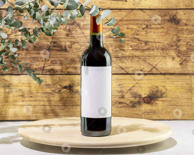 Скачать Бутылка с красным вином на деревянном подиуме напротив деревянной стены фотосток Ozero