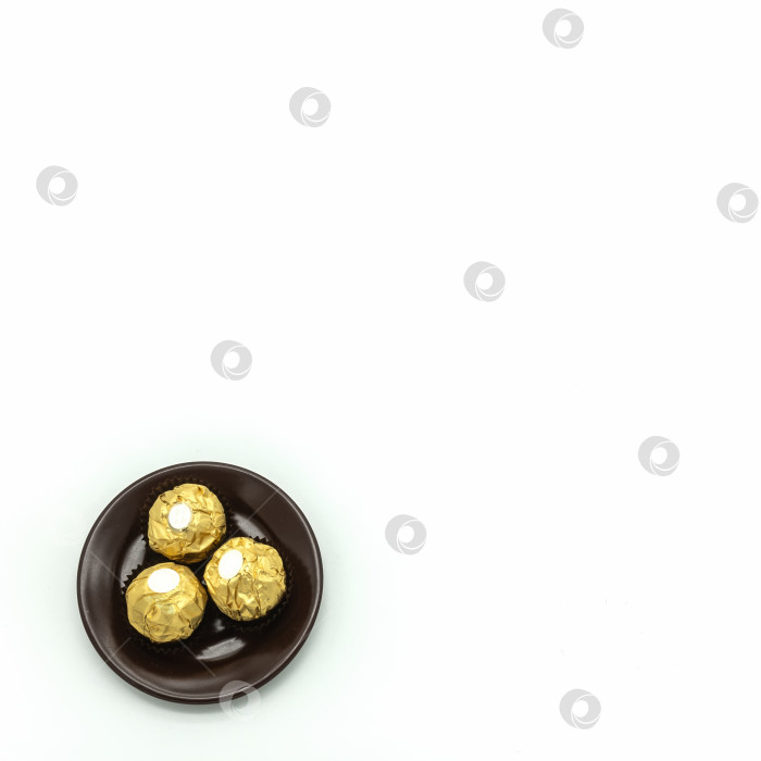Скачать Три шоколадные конфеты, завернутые в золотистую фольгу, лежат на коричневом фарфоровом блюдце. фотосток Ozero