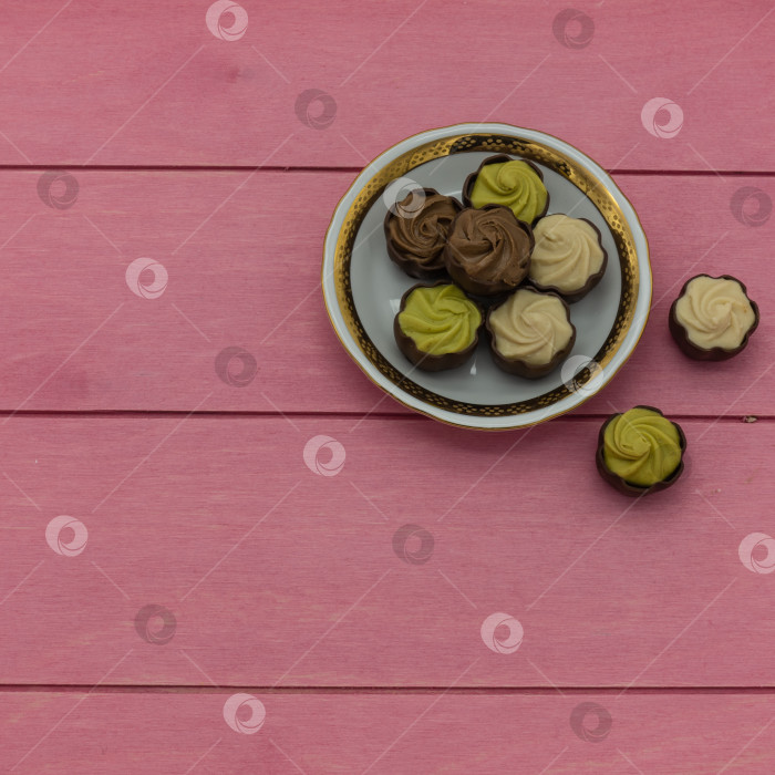 Скачать На белом фарфоровом блюдце с золотой каймой лежат шоколадные конфеты с фисташково-сливочной начинкой. фотосток Ozero