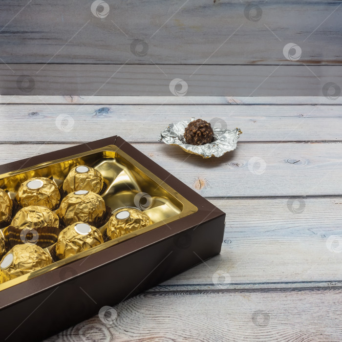 Скачать Коричневая картонная коробка открыта и наполнена шоколадными конфетами, завернутыми в золотую фольгу. фотосток Ozero