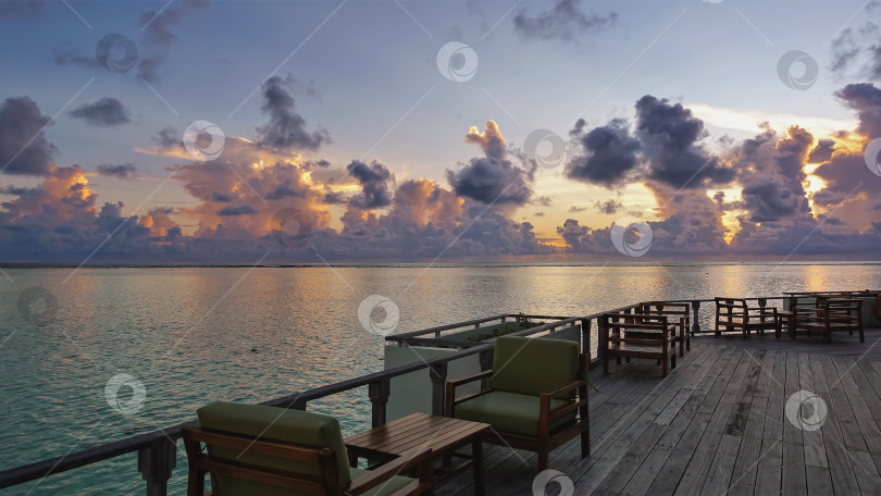 Скачать Вечер на Мальдивах. На деревянной платформе над океаном стоят столы и стулья. фотосток Ozero