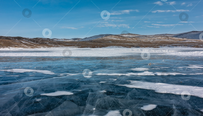 Скачать На гладком голубом льду замерзшего озера лежат пласты снега. Видны глубокие пересекающиеся трещины. фотосток Ozero