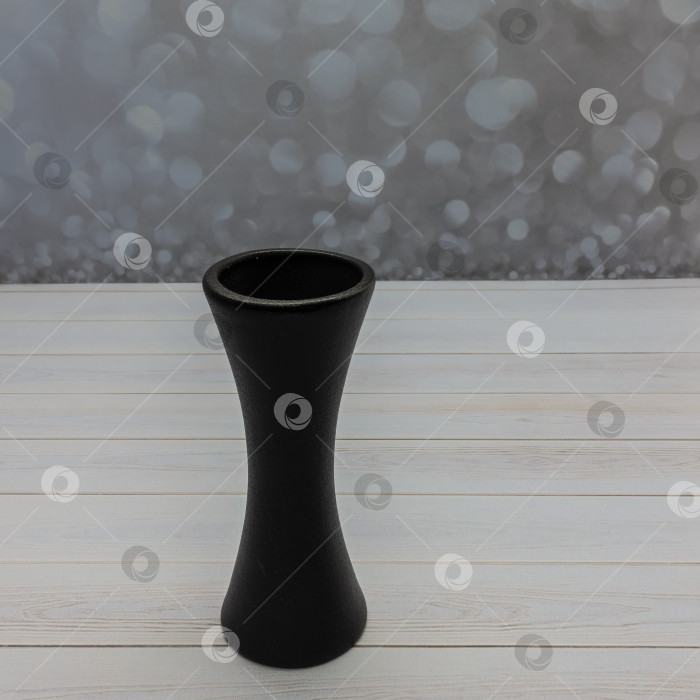 Скачать На деревянном столе стоит изящная керамическая ваза для цветов черного цвета. фотосток Ozero