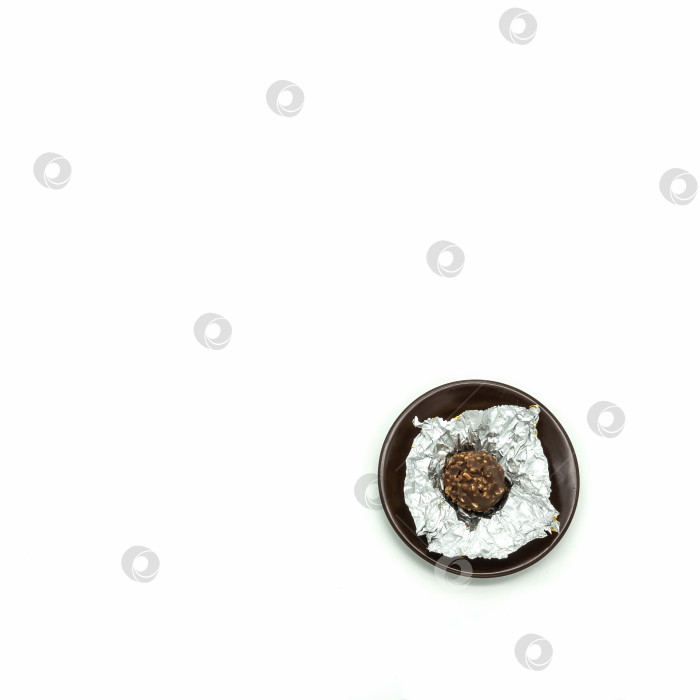 Скачать Шоколадно-ореховая конфета в серебряной фольге развернута и лежит на коричневом блюдце. фотосток Ozero