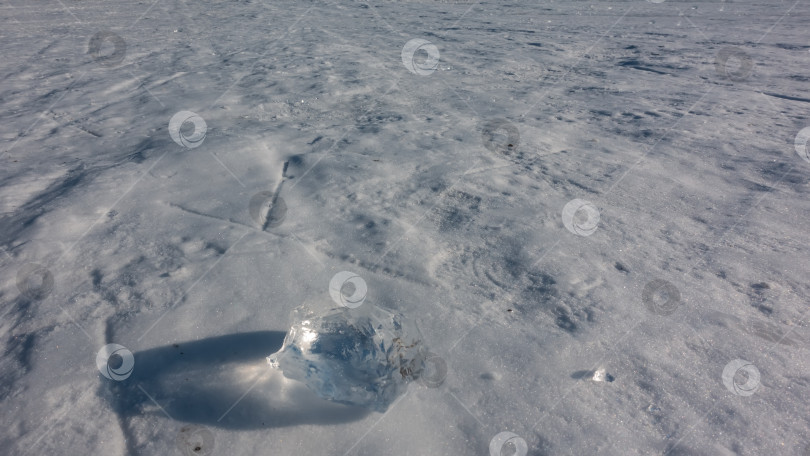 Скачать Прозрачный осколок льда лежит на замерзшем и заснеженном озере. фотосток Ozero