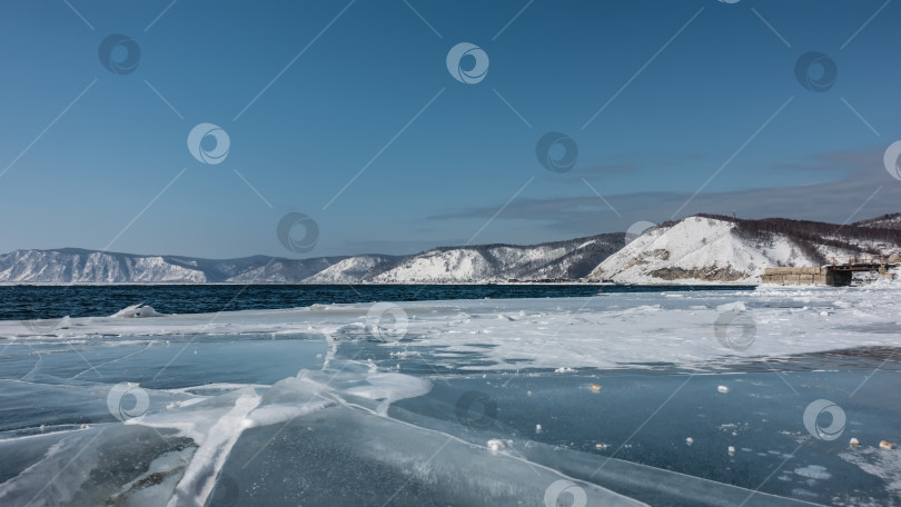 Скачать Голубая вода незамерзающей реки покрыта рябью. У побережья есть лед с трещинами и торосами. фотосток Ozero