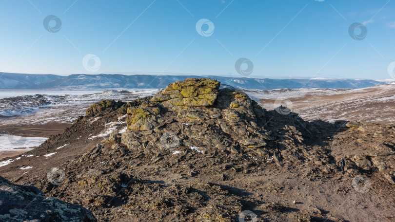 Скачать Зимний сибирский пейзаж. Желтые лишайники растут на потрескавшейся гранитной скале. Вдалеке вы можете увидеть горный хребет, замерзшее озеро. Чистое голубое небо. Байкал фотосток Ozero