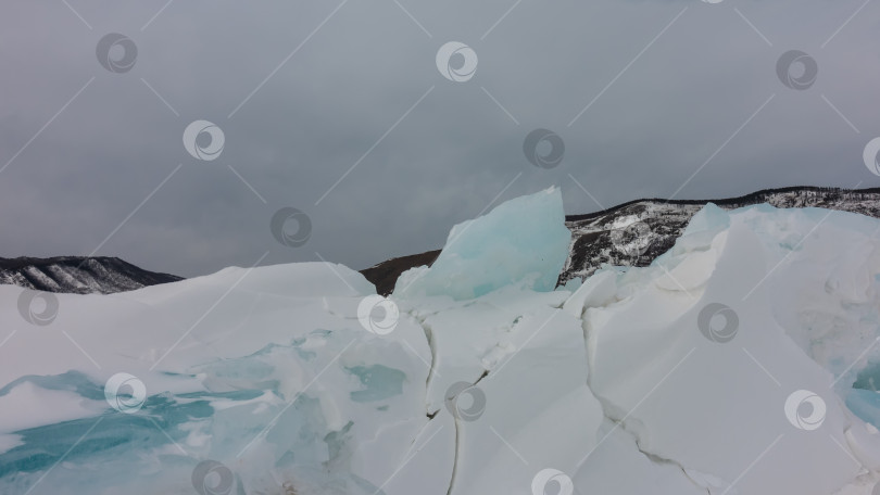 Скачать Бирюзовый лед и белый снег с трещинами на фоне пасмурного зимнего неба фотосток Ozero