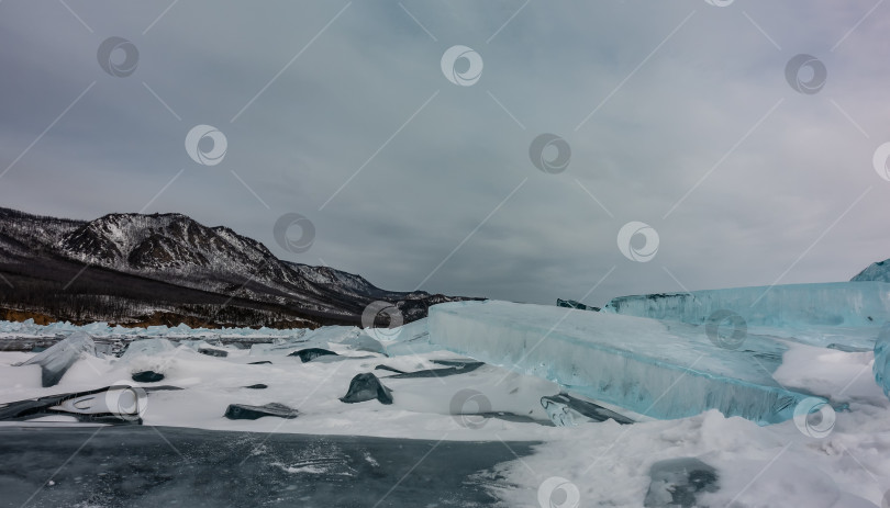 Скачать Глыбы бирюзовых льдин лежат на замерзшем озере. Снег на поверхности. фотосток Ozero