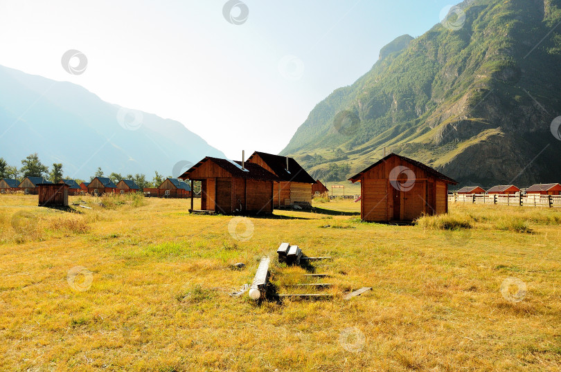 Скачать Небольшие гостевые домики в живописной долине, залитой солнечным светом, у подножия высоких гор. фотосток Ozero