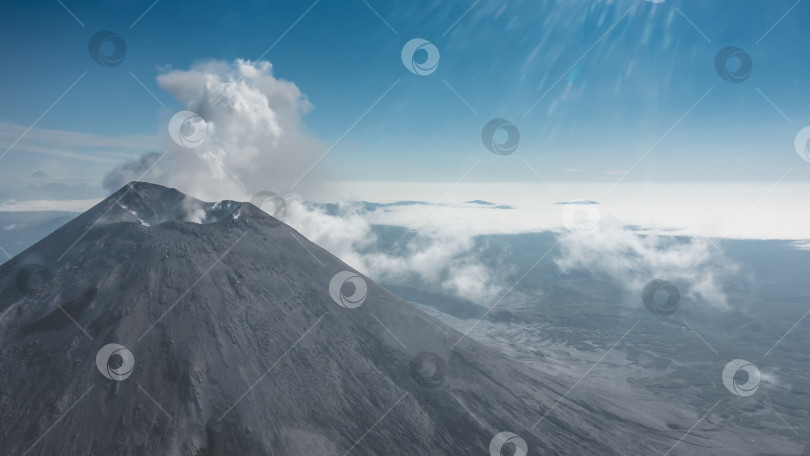 Скачать Над облаками возвышается конический стратовулкан. фотосток Ozero