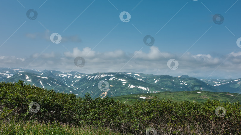 Скачать На горных склонах есть участки, покрытые снегом.  На переднем плане - холм с зеленой растительностью. фотосток Ozero