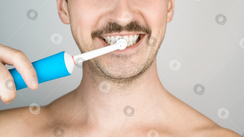 Скачать Мужчина со щетиной чистит зубы, ежедневная гигиеническая процедура. Портрет мужчины крупным планом с современной электрической зубной щеткой. Здоровье полости рта фотосток Ozero