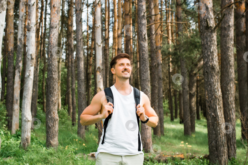 Скачать Мужчина гуляет на свежем воздухе. Красивый улыбающийся молодой человек с рюкзаком стоит в сосновом лесу и смотрит в сторону. Счастливый путешественник, отдыхающий на природе солнечным летним днем. Поход, путешествие, концепция треккинга фотосток Ozero