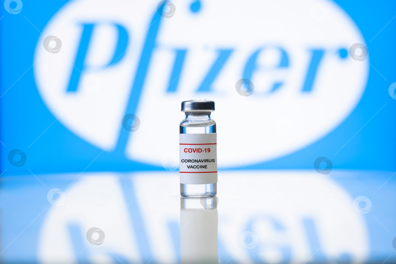 Скачать Вакцина Pfizer. Флакон с вакциной covid-19, на заднем плане логотип американской фармацевтической компании Pfizer. Концепция вакцинации. Россия, Смоленск 25.01.2021 фотосток Ozero