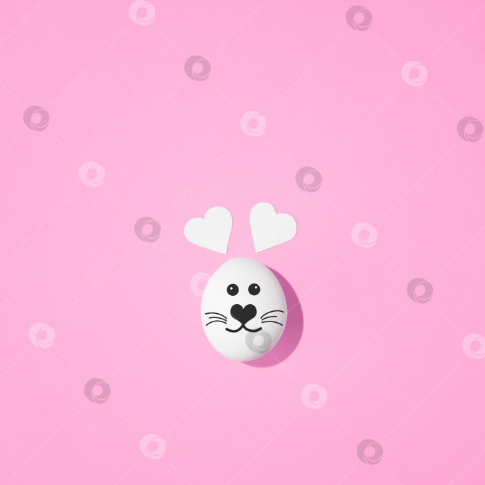 Скачать Креативная пасхальная концепция в стиле минимализм. Мордочка кролика, нарисованная на яйце, с ушками в форме сердца на пастельно-розовом фоне. Лежал плашмя. фотосток Ozero