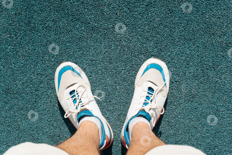 Скачать Вид сверху спортсмен в белых кроссовках стоит на резиновом покрытии открытой спортивной площадки. фотосток Ozero