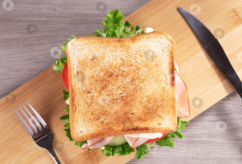 Скачать Вкусный сэндвич с ветчиной, свежим салатом и маринованным огурцом подается на деревянной доске. фотосток Ozero